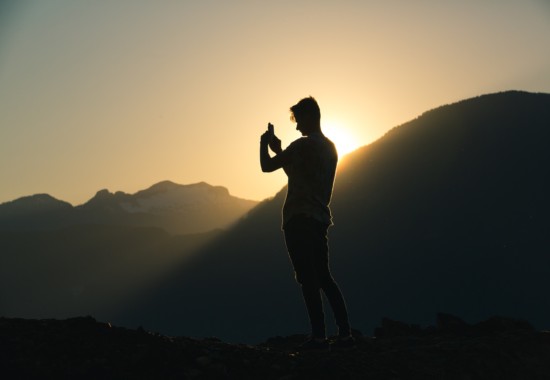 山頂から昇ってくる太陽の写真を撮る登山者